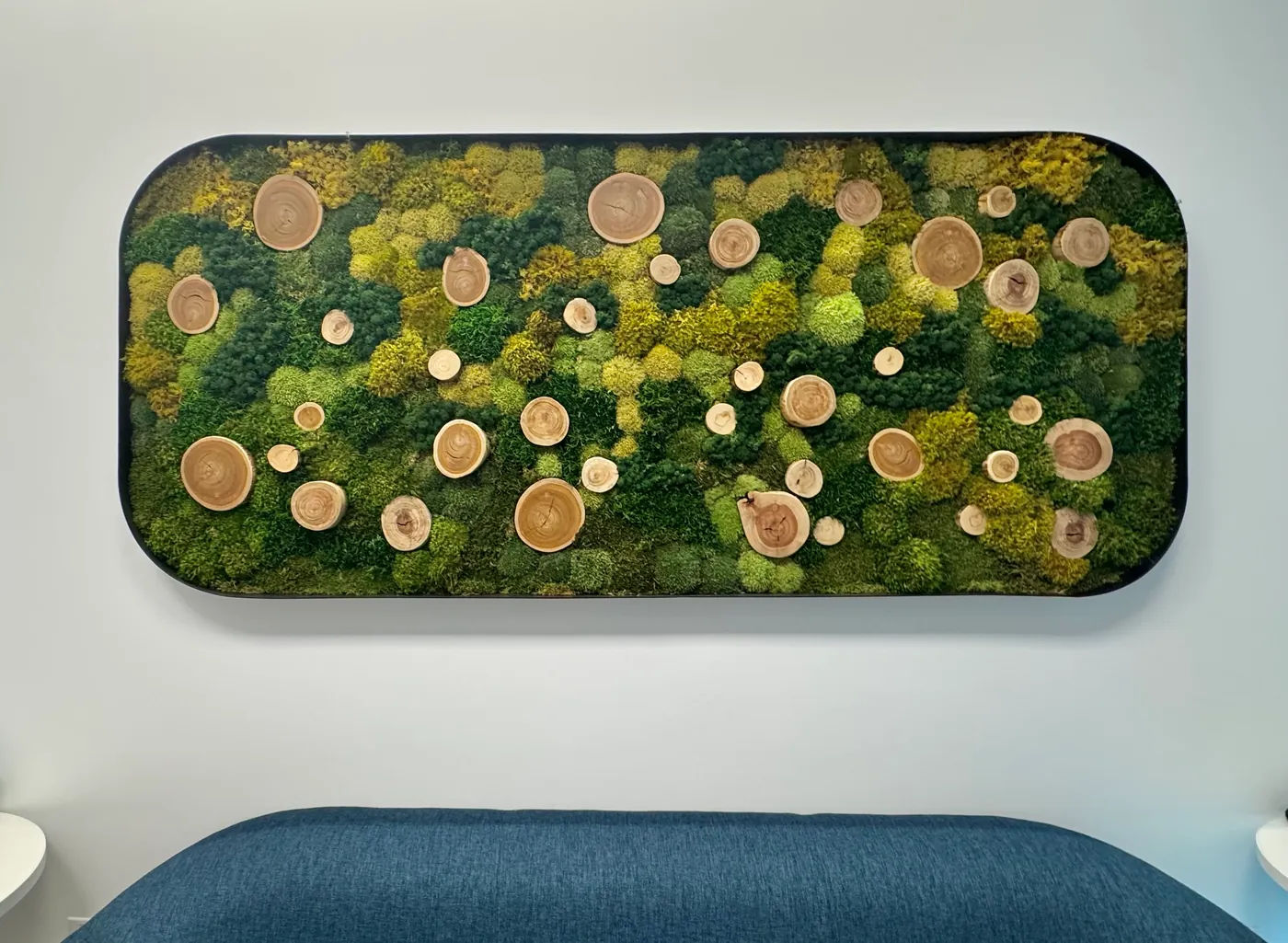 A moss panel with wood rounds above a sofa